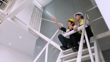 İç mimar proje planı ve mühendisi tutuyor. Merdivenlerde oturup proje sorununu konuşuyor..