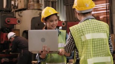 Laptop kullanan iki sevimli Asyalı kadın mühendis fabrikadaki verimliliği artırmak için işçilerin çalışma saatlerini iyileştirme planlarını tartışıyor..