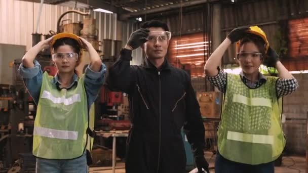 2人のかわいい女性エンジニアとシニア男性エンジニアは安全ヘルメットと眼鏡を着用し 腕を持ち上げ 男性エンジニアは親指を上げた 労働者と工場のコンセプト — ストック動画