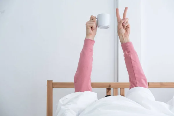 Erkek adam bir fincan kahve ve iki kolunu yatağın üzerine koyar. İnsanlar sabah hayat tarzı aktiviteleri yapar, tembellik eder ve uyanır ve kahve içer. Yatak odasında tatil tatili..