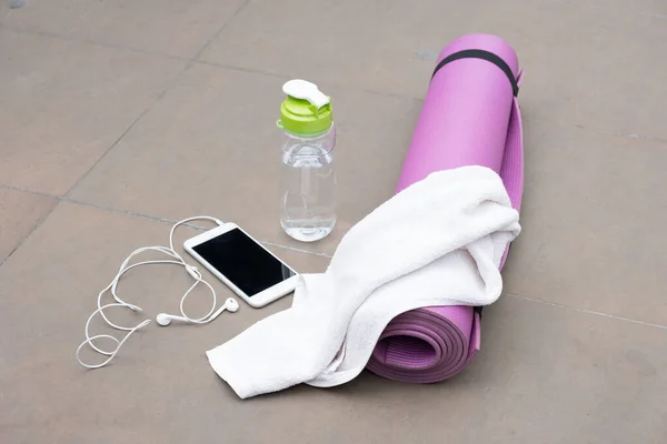 Akıllı telefon, su şişesi ve yerde beyaz havlu olan yoga minderi..