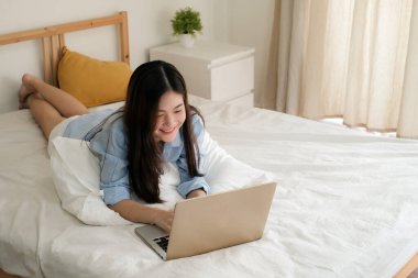 Mavi gömlekli tatlı Asyalı kadın evde çalışmak için dizüstü bilgisayar kullanıyor..