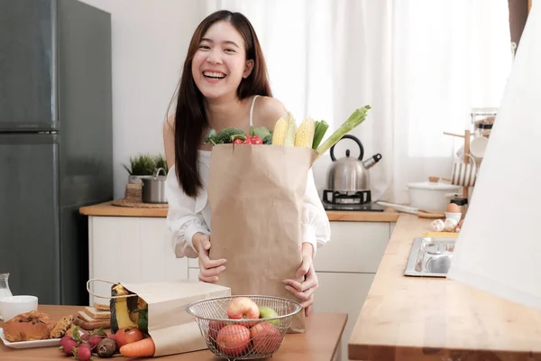Mutfakta kahvaltı için alışveriş poşeti tutan sevimli Asyalı kadın. Kameraya bak ve gülümse..