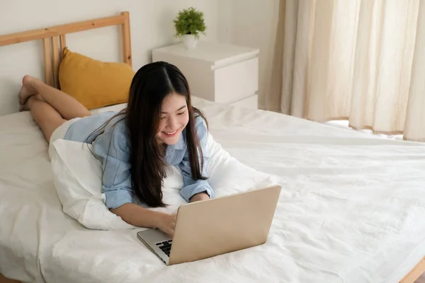 Mavi gömlekli tatlı Asyalı kadın evde çalışmak için dizüstü bilgisayar kullanıyor..