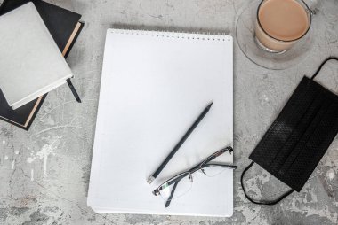 Siyah tıbbi maske ve defter. Bir fincan kahve ve bir kalemin yanında. Evden çalışıyorum. Karantinada evinizde kalın. Coronavirus konsepti /