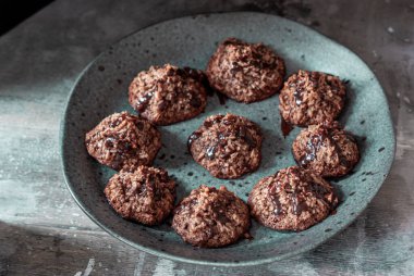 Kakaolu ev yapımı hindistan cevizi kurabiyeleri gri bir tabakta ve eski püskü ahşap arka planda. Siyah yemek fotoğrafı..