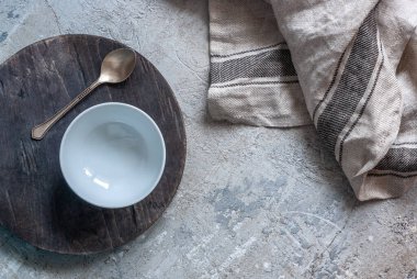 Beton bir atölyede tahta bir tahtanın üzerinde duran beyaz yuvarlak boş bir kase. Kopyalama alanı, mutfak kapağı.