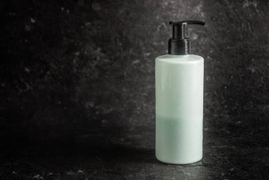 Siyah şapkalı beyaz-mavi şişe. Vücut için merhem, kişisel bakım. Siyah bir taş arkaplanındaki metin boşluğu.