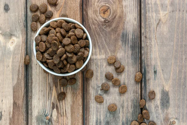 Granules of dry food for dogs and cats in a white bowl on a wooden table. Pet food