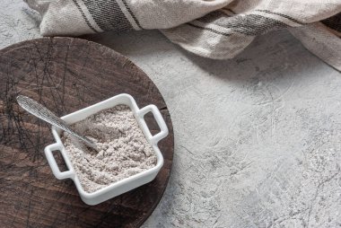 Beton masa arkasında tahta bir tahtanın üzerinde beyaz bir kasede kiraz unu. Mutfak kapağı, pişirme karışımı.