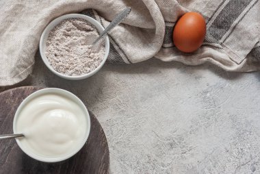 Kuş vişneli kek için malzemeler. Kuş kirazı, yumurta ve yoğurt ile bej havlunun yanındaki gri beton masada un karışımı. Kopyalama alanı pişirme tarifi