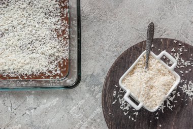 Chocolate cake with coconut shavings in a glass baking dish during cooking. Copyspace on a gray concrete table clipart