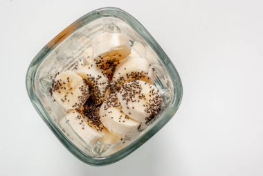 Meyve suyu için malzemeler. Beyaz bir zemin üzerinde muz ve blender içinde chia tohumları.