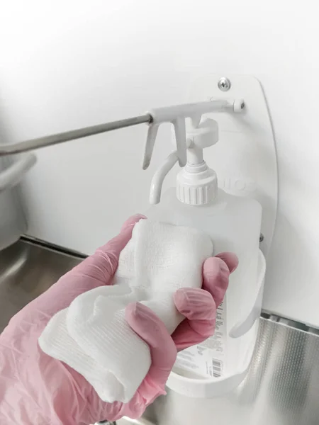 Dispenser for alcohol, disinfectant. Infection protection. Gauze in hand in a medical glove and a disposable surgical gown.