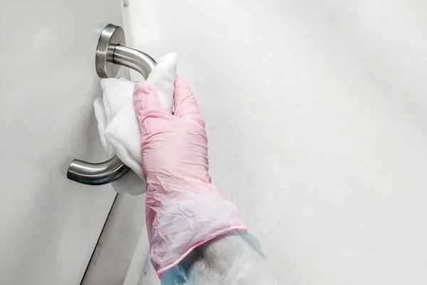 Cleaning surfaces and handles with alcohol. Infection protection. Gauze napkin in hand in medical glove and disposable surgical gown