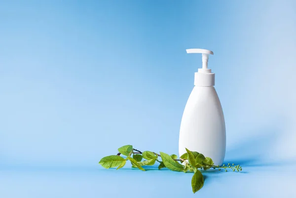 White bottle with a dispenser for liquid soap next to cherry leaves on a blue background. Body care, beauty copyspace