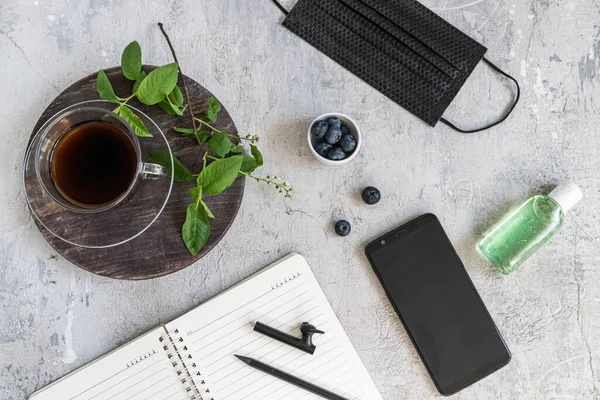 Evden karantinaya alınmış. Flatlay. Bahar, yeşil yapraklar, sade kahve, antiseptik yabanmersini ve tıbbi maske..