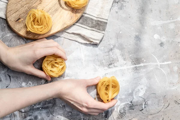 Italian nest pasta in female hands over a gray wooden table. Homemade copyspace recipes.