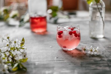 Kiraz çiçekleri ve yapraklarla dolu gri eski püskü bir masada bardakta limonata..