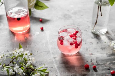 Bir bardak yaban mersinli limonata, buzlu ve böğürtlenli gri eski püskü bir masada çiçekler ve yapraklarla.