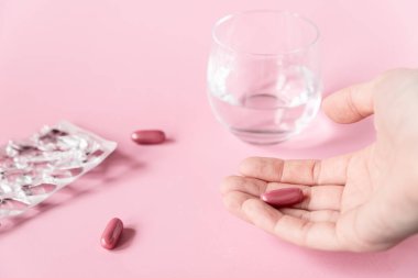Kız pembe arka planda vitamin kapsüllerini elinde tutuyor. Sağlık Hizmetleri