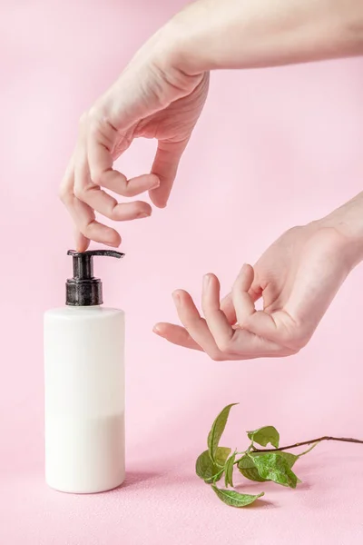 Girl clicks on a dispenser of skin care products on a pink background. Vertical Beauty Concept.