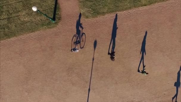 Schaduw van fiets en renner beweegt langzaam in het park. Ongewoon uitzicht vanaf top. — Stockvideo