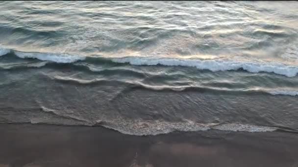 Pohled na oceánské vlny z vrcholu, hnědý písek a narůžovělé odrazy ve vodě při západu slunce — Stock video