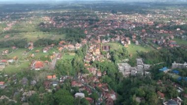 İnsansız hava aracı ubud üzerinde uçar, güneşli havada bali görünür kırmızı çatılar yeşillikte gömülü ve ubud yolunun ortasında Jl raya ubud