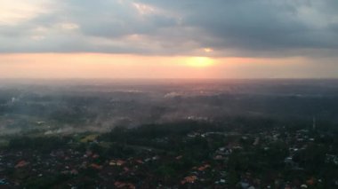 Kuadrokopter Bali 'deki Ubud ormanının üzerinden uçar ve gün batımına doğru uçar, tüm gökyüzü bulutlarda ve sarı-turuncu güneş görünür, her şey puslu