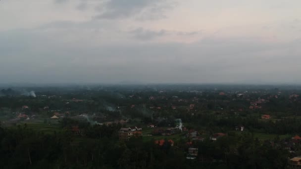 Quadrocopter flyger längs risfält snår av palmer är synliga på kvällen och röda tak av hus, rök från brasor är också synlig, vid horisonten allt är i en dimma — Stockvideo