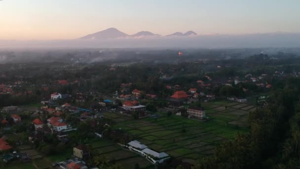 Quadrocopter dolly volando sobre Ubud Bali, y muchas casas con techos rojos, montañas en el horizonte y un globo con nubes pintorescas y cielo azul — Vídeo de stock