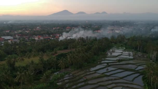 Prachtige zonsondergang met drone vliegen weg over Ubud Bali, en vele huizen met rode daken, bergen aan de horizon met blauwe lucht — Stockvideo