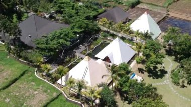 Bir kuadrokopter Ubud Bali 'deki chi piramitleri boyunca uçar, ormandaki palmiye ağaçları ve piramitler açık güneşli havada mavi gökyüzüne ve pirinç tarlalarına karşı görünür.