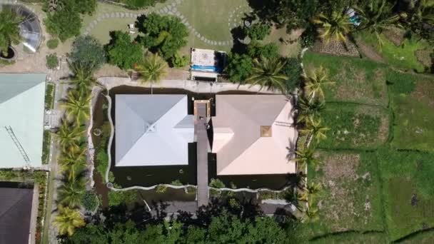 Drönaren flyger långt upp från pyramiden omgiven av vatten i Ubud Bali, i klart soligt väder syns tropiska palmer och risfält runt — Stockvideo