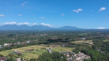 Ubud 'un merkezindeki gökyüzünde beyaz bulutlu, güneşli bir havada görünen dağların arasında, pitoresk bir ormanda uçmak.