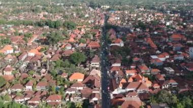 Ubud jl.Raya Ubud 'ın merkezinde uçan mobiletlerin ve arabaların hareketini görebilirsiniz. Güneşli havada, kırmızı çatıları olan evler.
