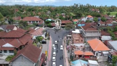 Güneşli havada COK Gede Rai ve Raya Ubud bali kavşağında ArJUNA heykelinin üzerinde uçan arabalar ve scooterlar görülebiliyor.