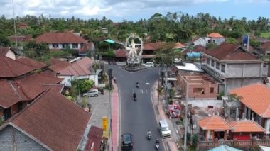 Güneşli havada COK Gede Rai ve Raya Ubud bali kavşağında ArJUNA heykelinin üzerinde uçan arabalar ve scooterlar görülebiliyor.