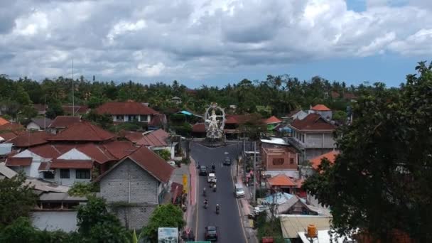 Vliegen boven het ARJUNA standbeeld, passerende auto 's en scooters zijn zichtbaar op de kruising van COK Gede Rai en Raya Ubud bali bij zonnig weer — Stockvideo