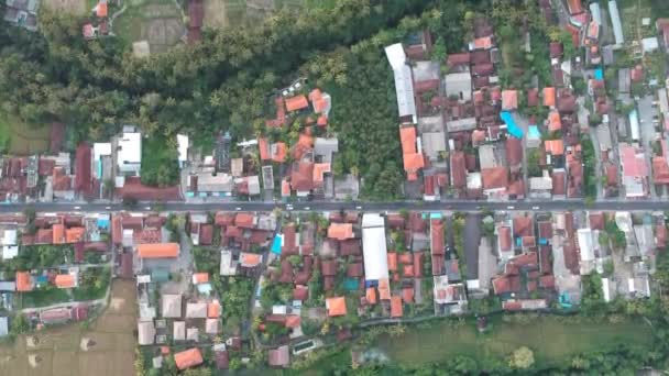 Vuelo sobre la calle Ubud a lo largo del cual los coches scooter y motocicletas paseo, tejados y un lecho de río con palmeras son visibles — Vídeo de stock