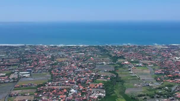 从上往下看阳光明媚的巴厘岛，可见红色的屋顶，绿色的稻田和大海背景 — 图库视频影像