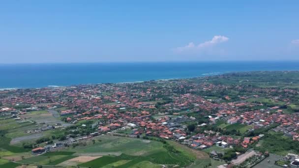 Panorama rapide vers le bas par temps ensoleillé donnant sur les rizières et les toits rouges des maisons sur le fond de l'océan bali indonesia — Video