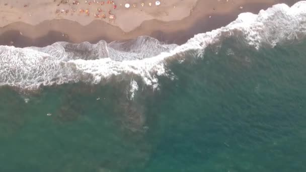 Flight over the blue ocean with big waves and people sunbathing under umbrellas and a hotel — Stock Video