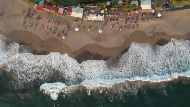 Gün batımında Canggu 'daki kumsala doğru statik bir çerçeve ve büyük dalgalarla deniz kenarında güneşlenen insanlar. — Stok video