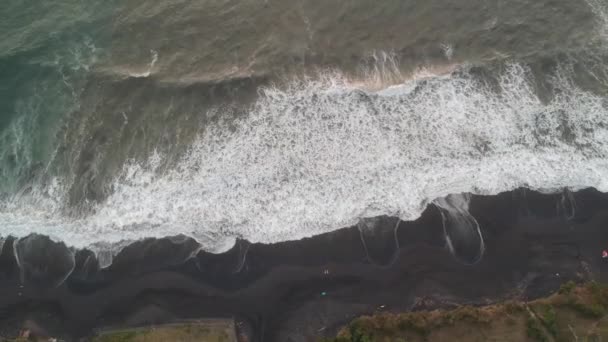 Flying high up above the beach with black volcanic sand, large waves and black water are visible — Stock Video