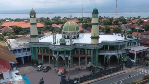 Dron odlatuje od meczetu Al-Mubarok Grand pokazuje morze w tle i drogę z samochodami i skuterami Gilimanuk Melaya West Bali Indonesia — Wideo stockowe