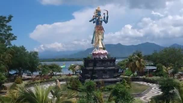 Güneşli havada Shiva Taman Siwa Anıtı 'nın önünde bir İHA ile dağların arka planına ve suya karşı havalan Gilimanuk Melaya Batı Bali Endonezya — Stok video