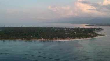 Gün batımında gili havasından hızlı bir şekilde ayrılan sahildeki tropiklerde ve güneş pansiyonlarında boğulan kafeleri ve arka plandaki Lombok adasını görebilirsiniz.