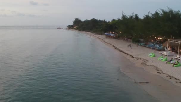Sulla costa con una spiaggia sabbiosa la sera e le luci di un caffè gili air indonesia — Video Stock